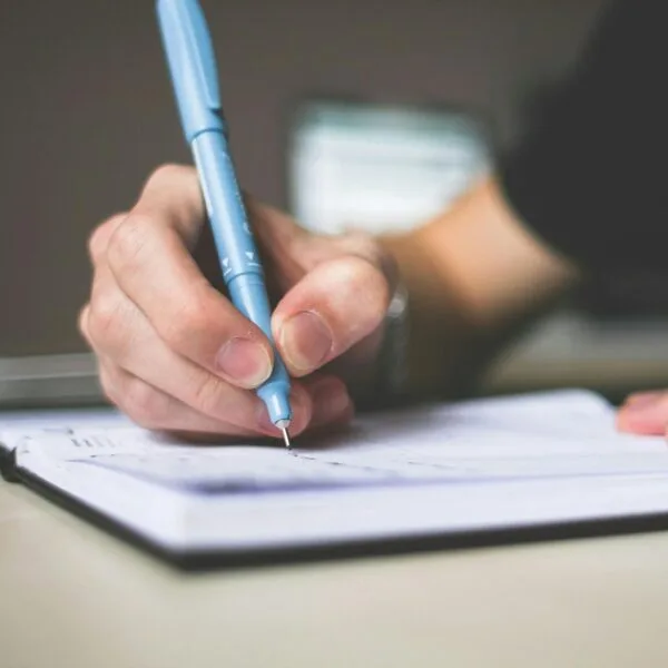 Hand holding a blue pen writing in a notebook