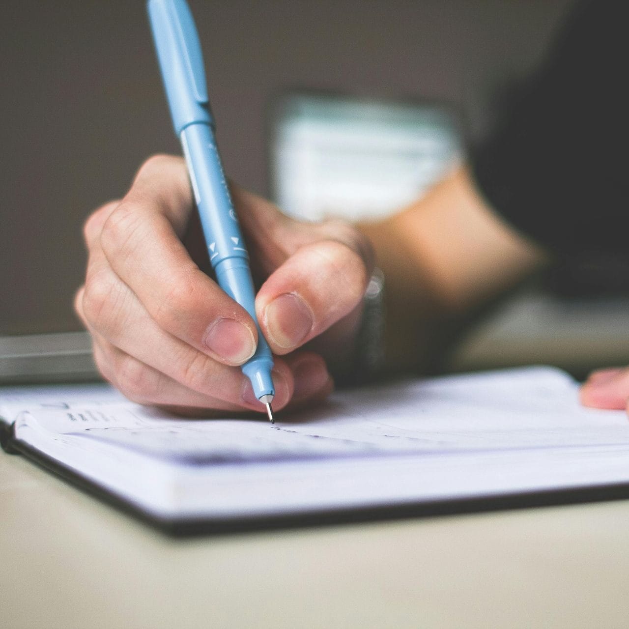 Home 11 Hand holding a blue pen writing in a notebook