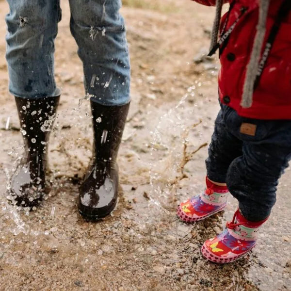 An adult and a child both wearing boots and getting splashed with water