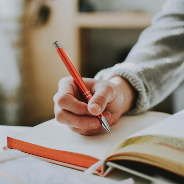 A person writing in a notebook with a red ballpoint pen, showcasing detail and focus.