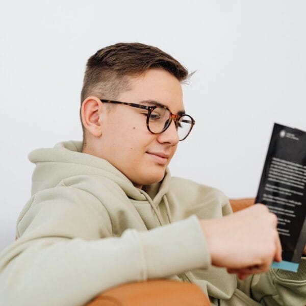 A young man wearing glasses enjoys reading a book while relaxing indoors.