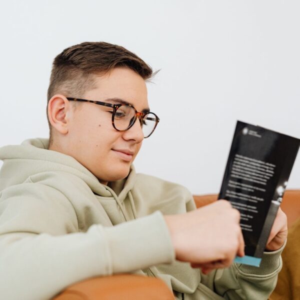 A young man wearing glasses enjoys reading a book while relaxing indoors.