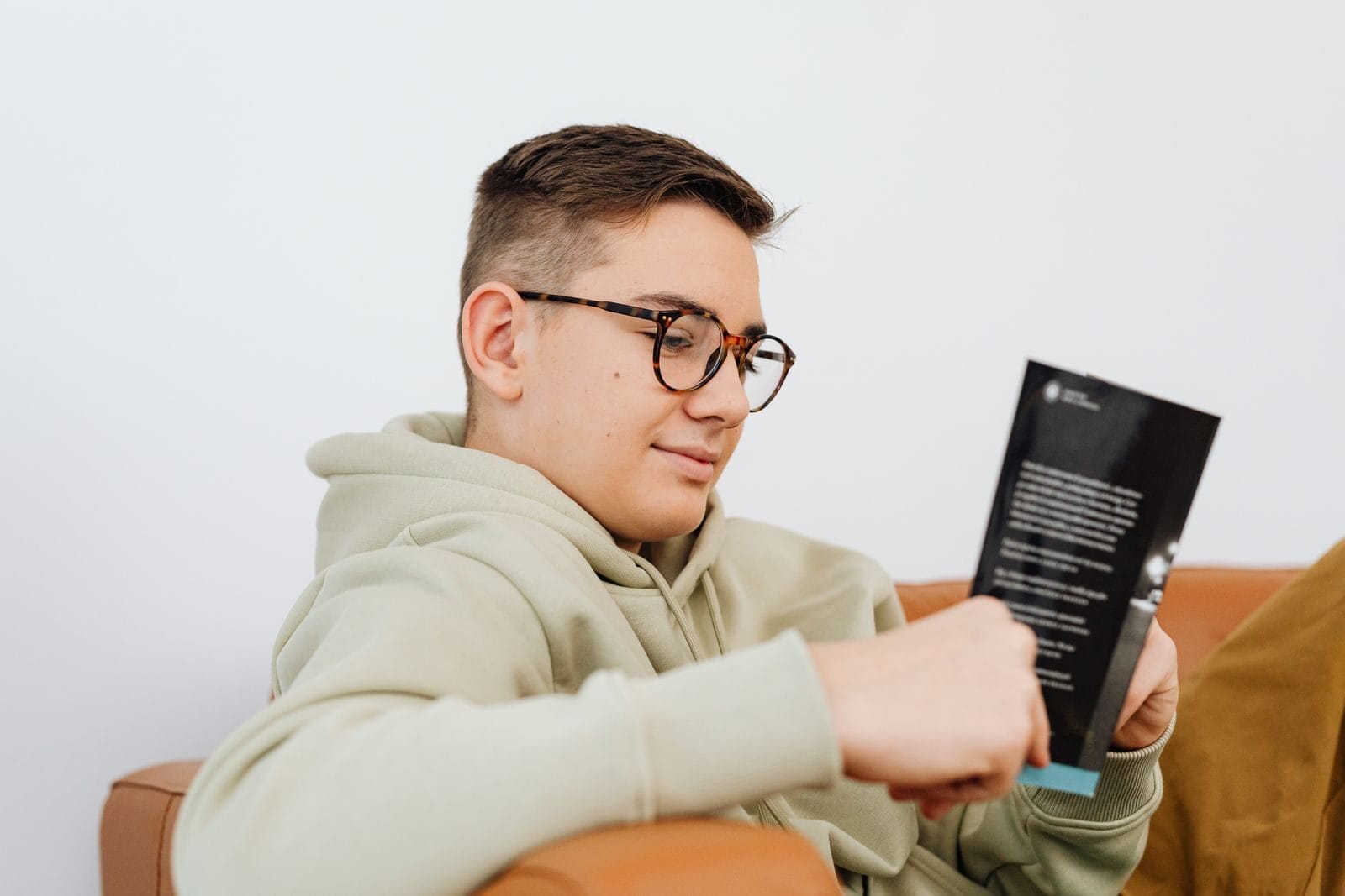 A young man wearing glasses enjoys reading a book while relaxing indoors.