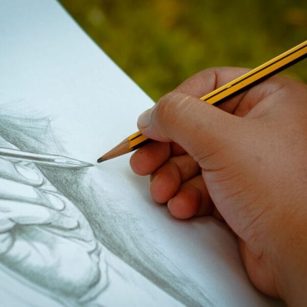 A close-up view of a hand sketching with a pencil on paper. Ideal outdoor art scene.